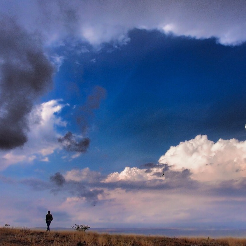 distance view of man walking in a field beneath a vast sky